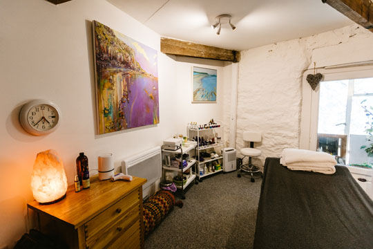 photo of massage studio with massage bed, side table with salt lamp and massage oils